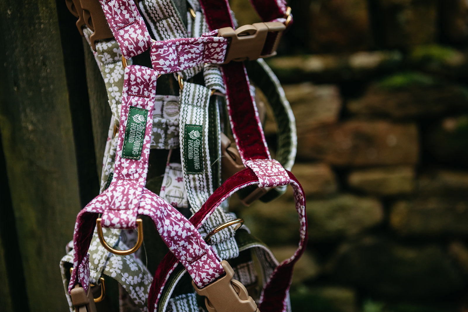 Blooming Hound strap-only dog harnesses with patterned straps hanging against a stone wall.